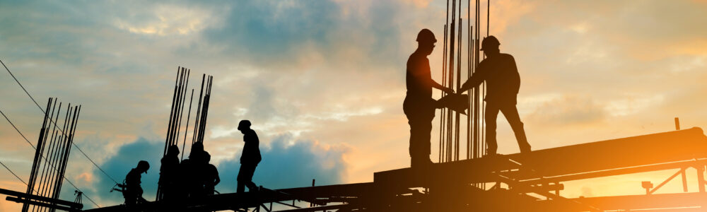 A silhouette of seven construction workers working onsite as they build a new industrial facility.